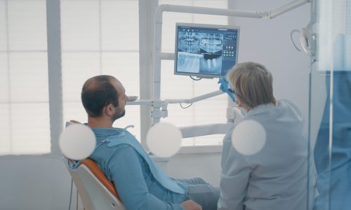 Mature dentist pointing at teeth radiography on monitor