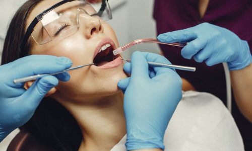 The dentist treats the girl's teeth. A young woman visited a dentist. The doctor works with an assistant